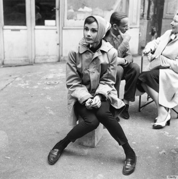 Actress Audrey Hepburn (1929 - 1993) sitting on a crate near the Eiffel Tower in Paris, during the filming of 'Funny Face', 1956. Co-star Fred Astaire (1899 - 1987) is behind her. (Photo by Paramount Pictures/Getty Images)